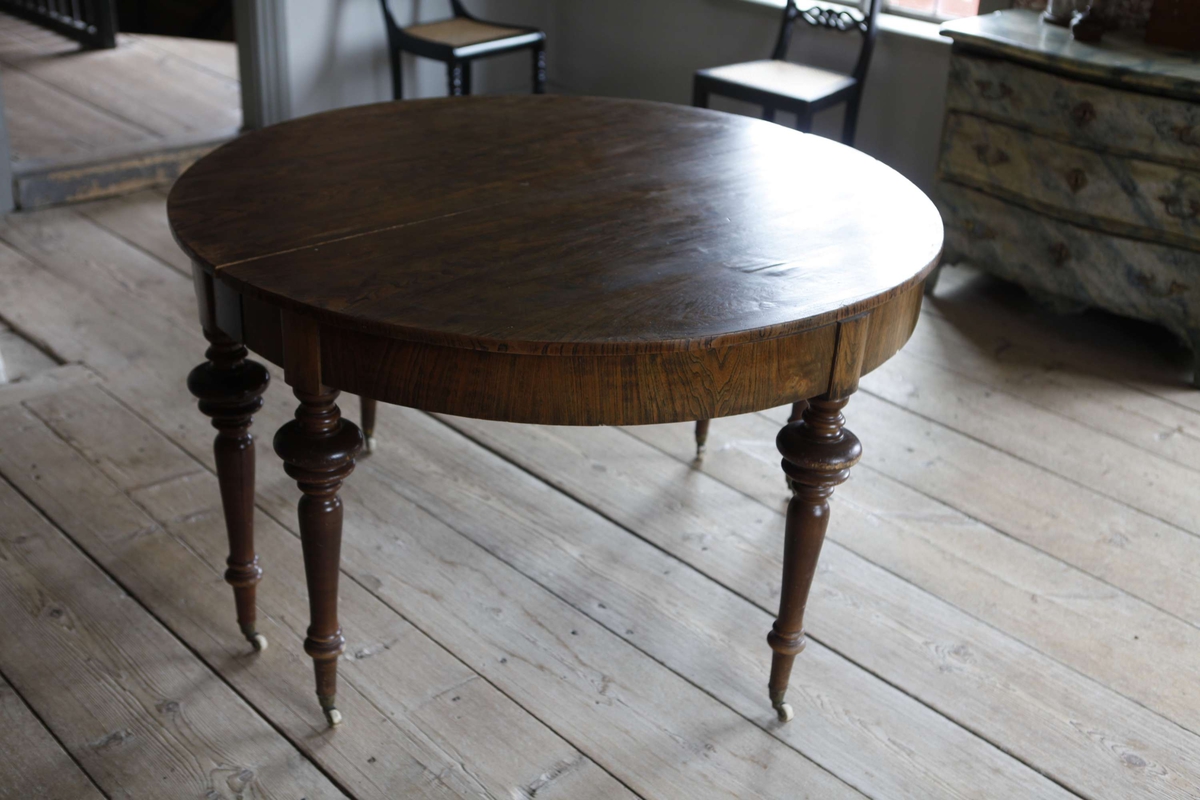 Matsalsbord av bonad alm. Hjul av mässing. Till bordet hör två skivor 115,5 x 55,5 cm och två stöd, 78 cm långa, av obehandlat trä.

