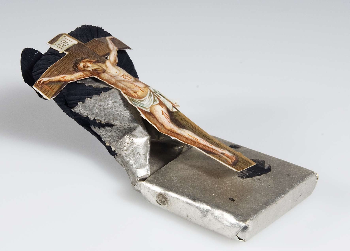 Begravningskaramell, omslag av silverpapper. Frans av svart crêpepapper. Bild av korsfäste Kristus i färg.