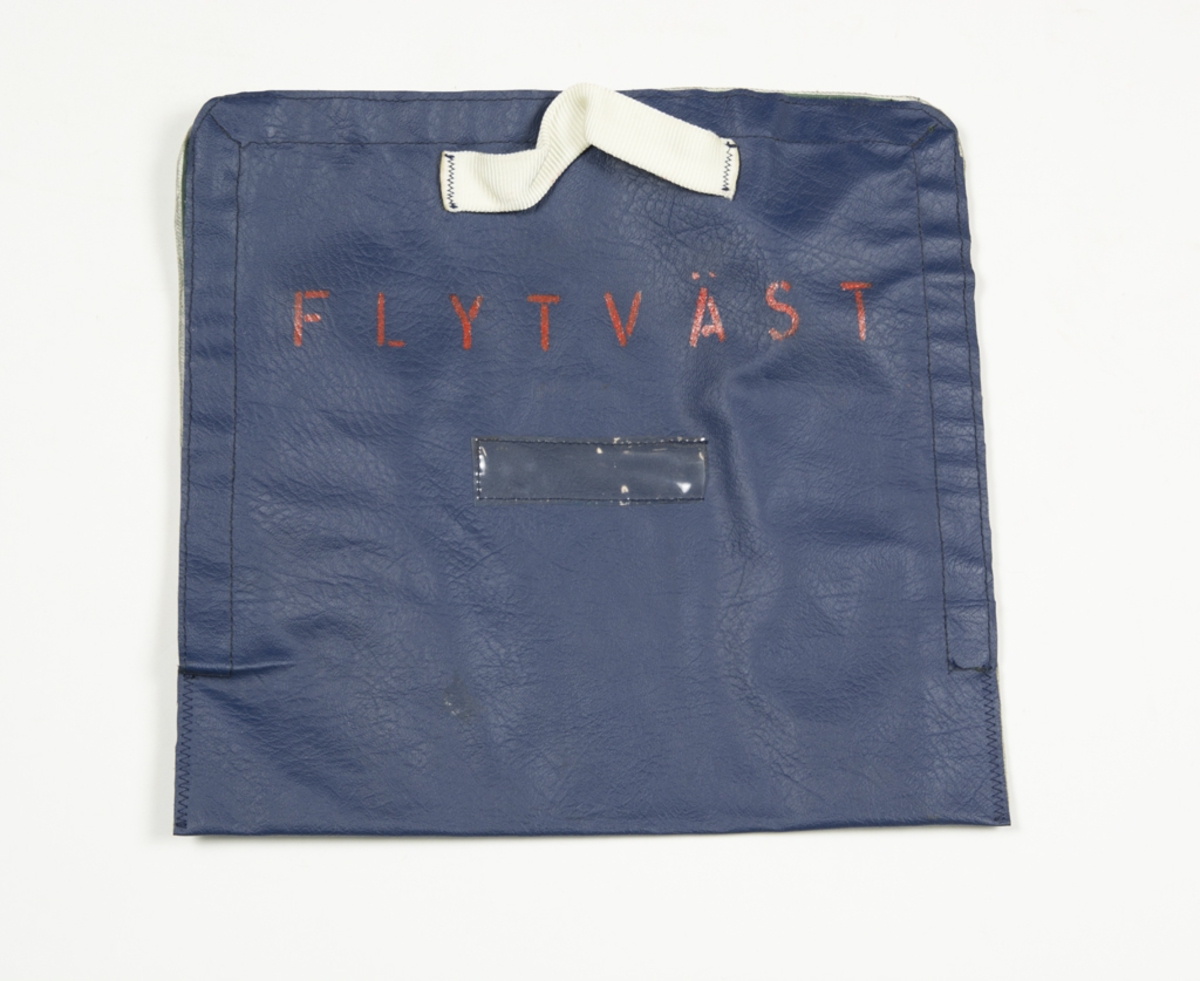Blå packväska för flytväst i kabin på transportflygplan. Väskan fästes ihop med kardborreband runt tre sidor , handtag i vit nylon. På framsidan står det skrivet Flytväst i rött. Väskan fästes med två kardborreband.
