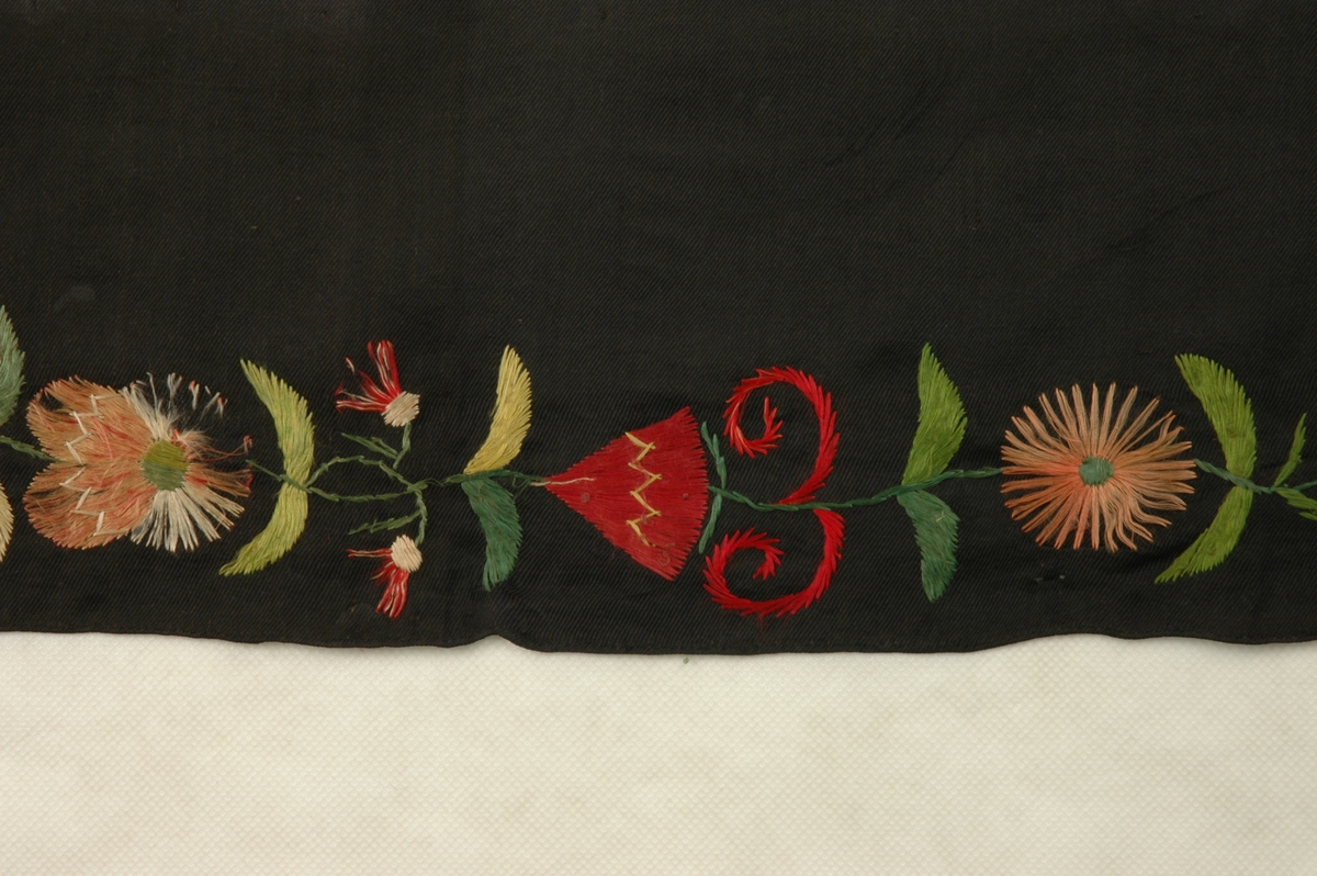 Kvadratisk tørkle i svart silke med påbroderte blomstermønster. To sider har fargerikt mønster, mens den andre har kvitt mønster.