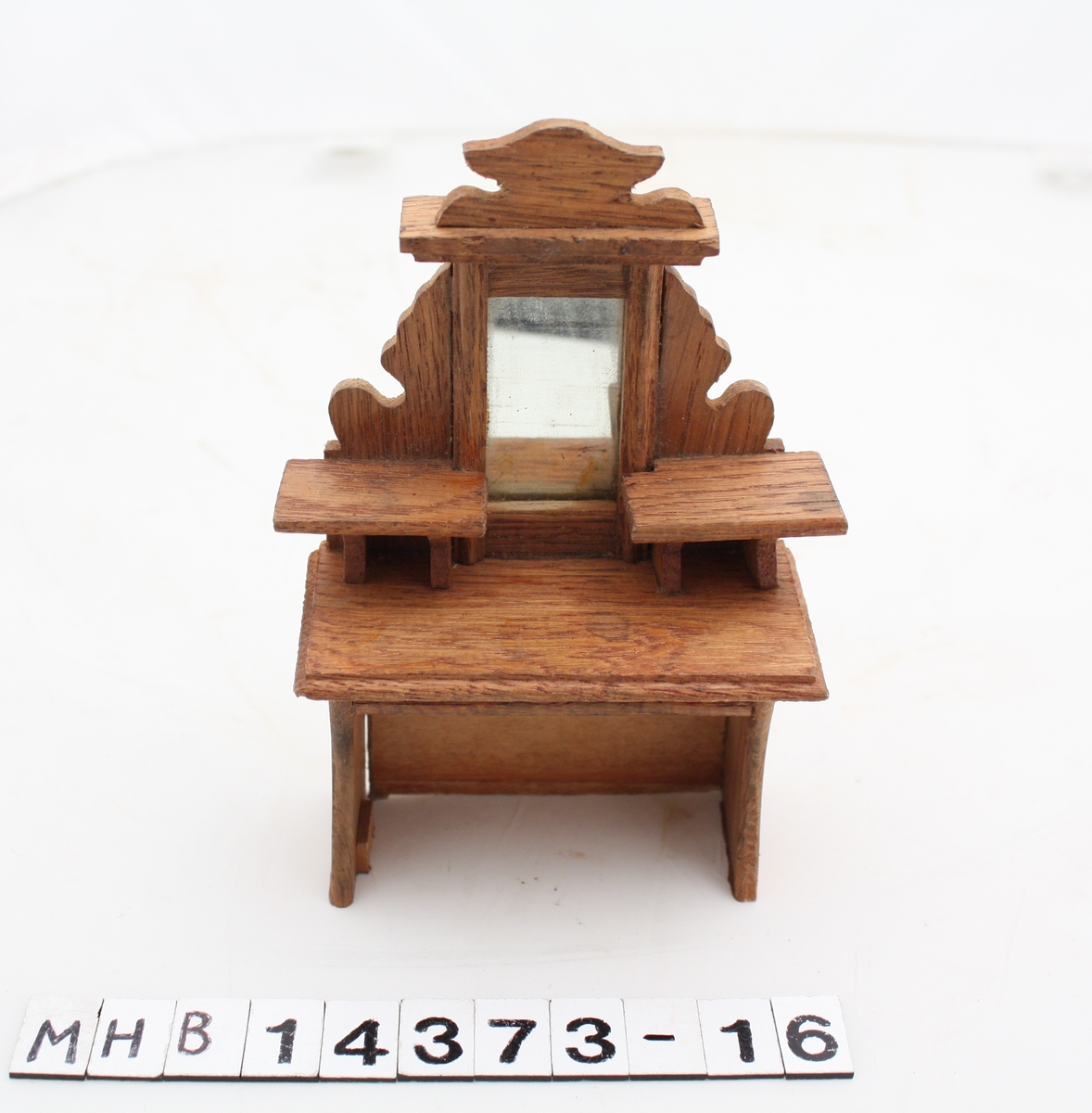Skrivebord i miniatyr til dukkehus. Bordplaten er rektangulær. Over bordplaten er et speil med to hyller på hver side.