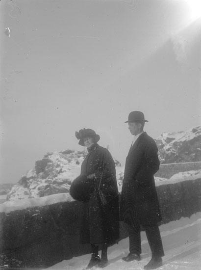 En kvinna och en man står längs vägen mot Hästepallarna, solen syns i övre högra hörnet och marken är täckt av snö. Kvinnan bär kappa, hatt och muff, mannen rock och hatt.