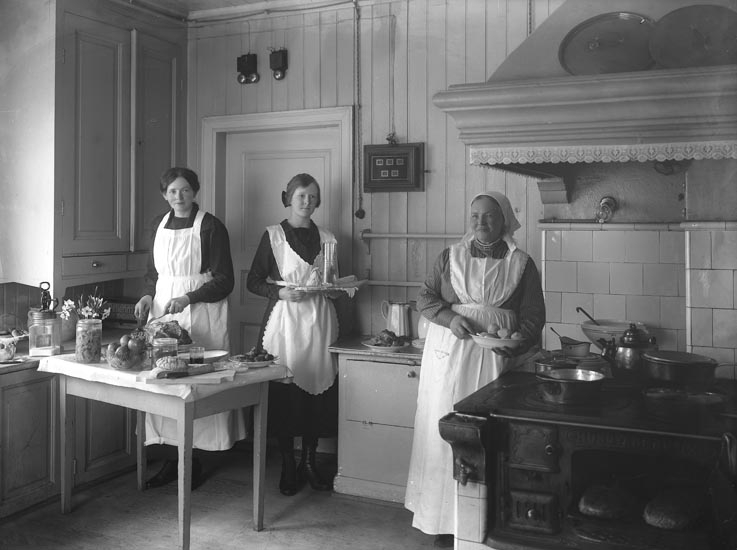 Enligt medföljande noteringar: "Köket. Gamla Fru Johansson gift med kusken på Herrgården o. Fröken Ida Larsson Marie (?) och hembiträdet fröken Rut Löfsten, omkring år 1930?" 

Se även UMFA53666:1320