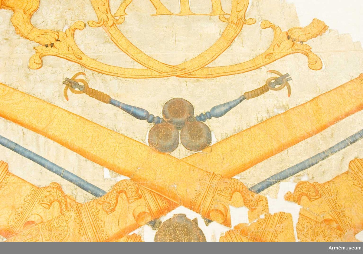 Grupp B.

Duk av vit damast, varå är målat, lika å båda sidor, ett stort rikt dubbelt C, omslutande XII, under en stor, sluten kunglig krona, allt i guld med något silver, kronan med blått foder, synligt även å bakre byglarna, och stenar i rött. Det hela uppbäres av tvenne gyllene, med slutna kronor krönta, dubbelsvansade lejon som stå på en grupp av två korsade gyllene   kanoner med Carl XII:s namnchiffer, tre kanonkulor i silvergrått, tvenne luntstakar i blått med brinnande luntor, två mörsare i guld, tre granater i silvergrått samt två luntpikar med blå stänger och bladen prydda med Carl XII:s namnchiffer, i hörnen "tre kronor" i guld med blått foder och pärlor i silver, i kanten utom och över lejonen fyrkulor i silvergrått med fem lågor i guld och rött, fäst med vitt sidenband och förgyllda spikar.

Bandet fortsätter lindat 150 mm ned på stången. Stång av furu, målad blå. Längd 3490 mm, diameter upptill  330 mm, nedom duken 530 mm. Spets av förgylld mässing, holk rikt profilerad. Dukens ovanligt stora dimensioner förklaras av att fanan var ämnad att föras på vagn (Cederström?).

"Inneliggande är en del av den stora fana, som  svenska artilleriet förde i slaget vid Narva, efter att kortt  förut hafva erhållit den som en present af Carl den 12te - Den  förvaras Tygförrådet". Papperet har en vattenstämpel.
