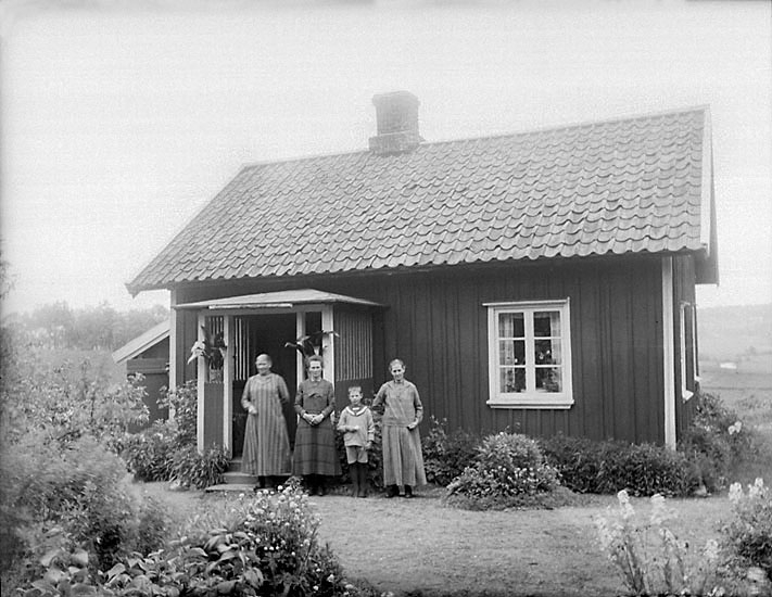 Tre kvinnor och en pojke i sjömanskostym, står framför verandan till ett bostadshus.