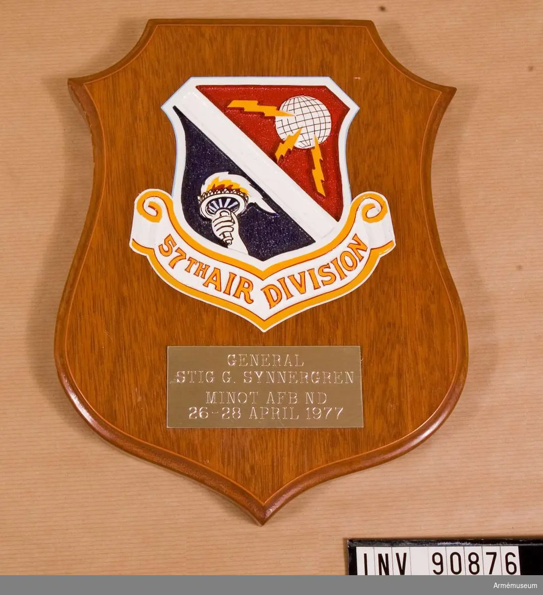 Fästade mot en sköldformad träbotten är 57th Air Divisions märke och en platta med ingraverad text.