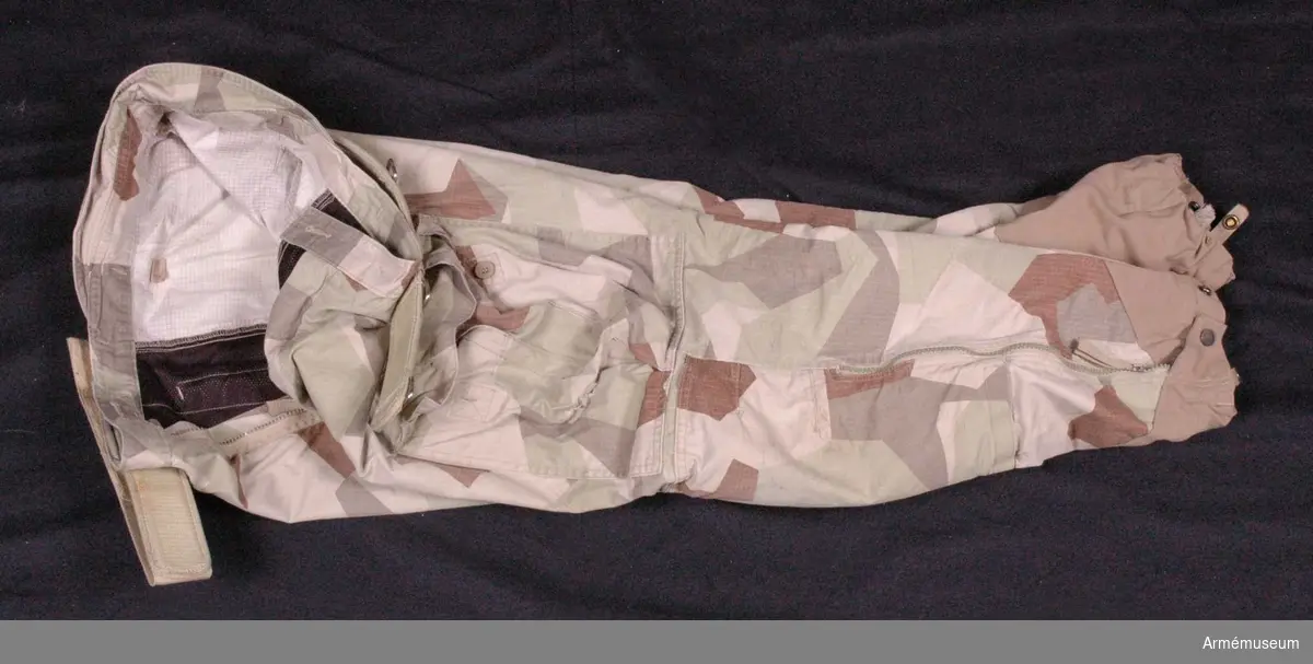 Utförda i ökenkamouflage.
Tillverkade 2009 i Kina.
På byxorna sitter en livrem (AM.096023).
Med tillhörande knäskydd.