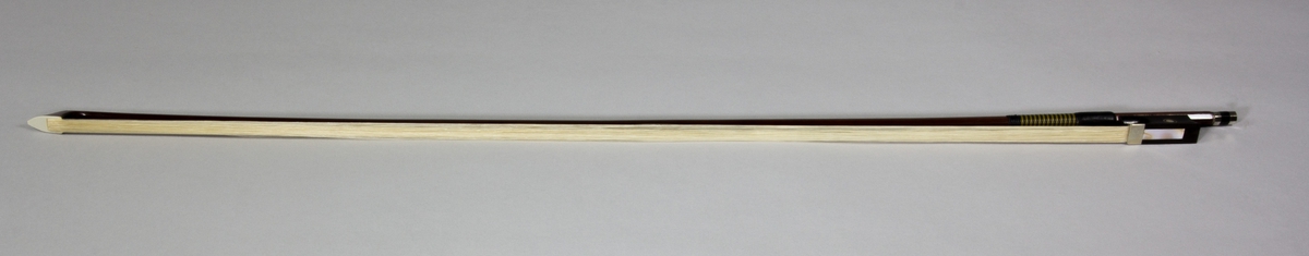 Stråke, fiolstråke, tillverkad av rödbrunt trä med ljust tagel. Vanlig modell med frosch och skruvspänning.