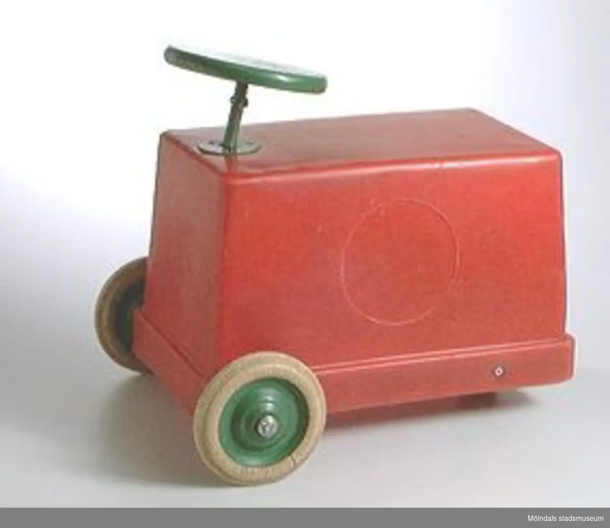 Röd åkbar leksaksbil i röd plast. Svartmålad träratt och gummihjul.