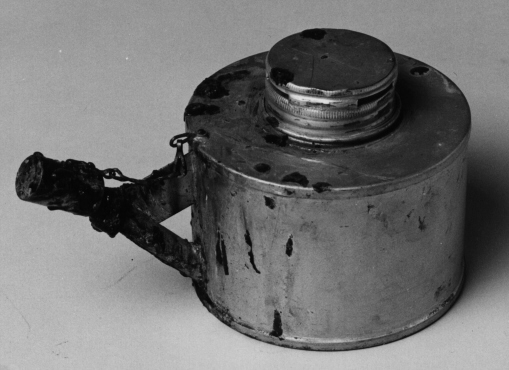 Förseglingslampa av gråmålad metall, för T-sprit.
Medlackrester. Använd för försegling med lack på Postmuseum,
Stockholmfrån ca 1970. Artikelnummer 662.10.
