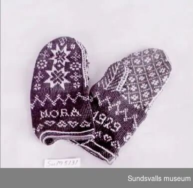 Ett par bruna mönsterstickade tumvantar med beige mönster i form av bl.a. stjärnor, hjärtan och texten 'MORA 1929'. Enligt anteckning ska vantarna vara tillverkade i tvåändsstickning.