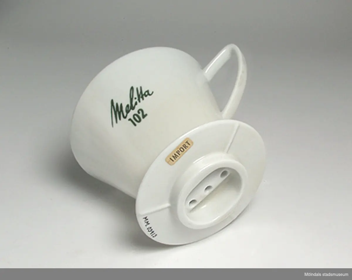 Vit hållare för kaffefilter Melitta 102. På undersidan sitter en lapp med texten: IMPORT.