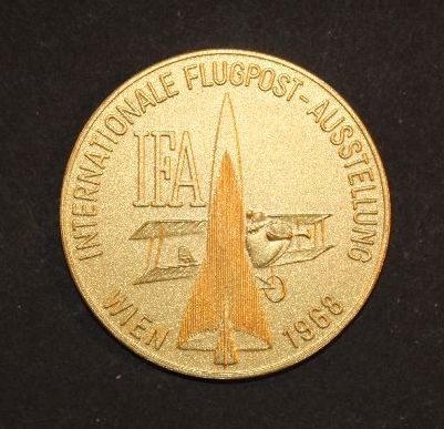 Medalj i förgylld mässing, rund. Åtsidan visar
flygplan(biplan) samt en raket och text enligt MRK. Medaljen
tilldeladPostmuseum för deltagande i utställningen IFA 1968 i Wien,
Österrike19680530 - 19680604.