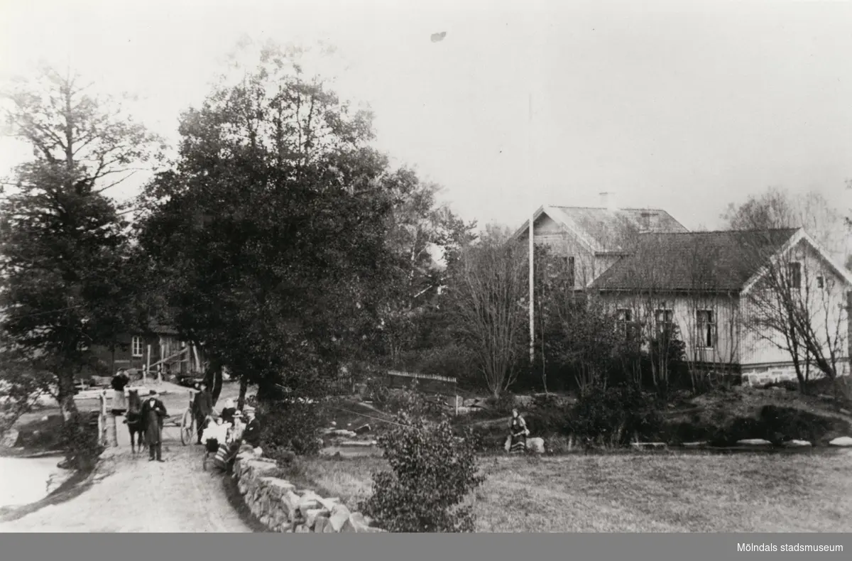 Hällesåkers bro i Lindome, 1907. Liten folksamling samt häst med kärra på bro.