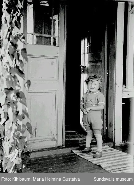 Porträtt, barn står i dörröppningen till bostaden.