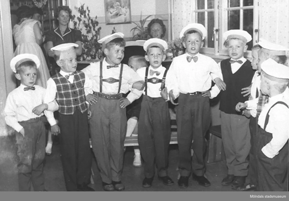Sånguppvisning av finklädda pojkar med vita mössor, som står arm i arm. Holtermanska daghemmet, okänt årtal.