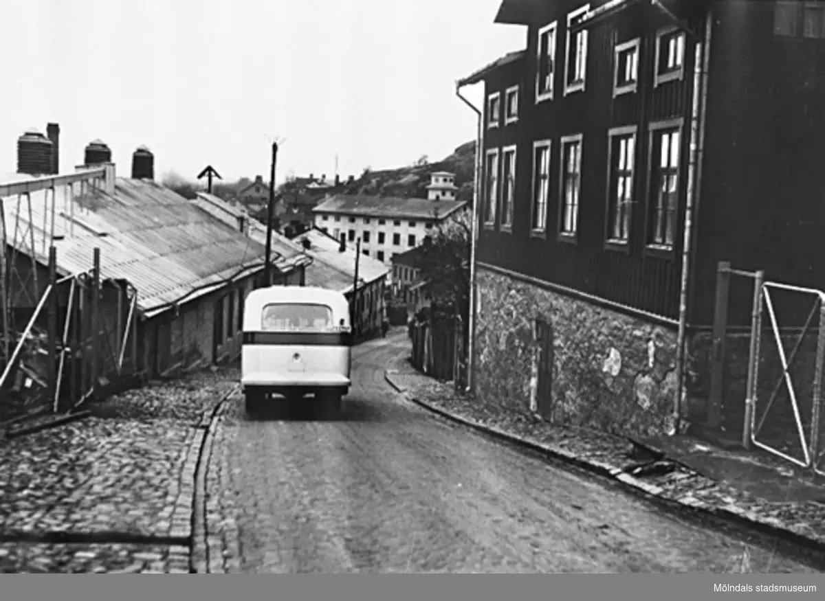 En buss som kör nedför "Mölndals Kråka" Kvarnbygatan, omkring 1938. På ömse sidor finns SOABs fastigheter. Det stora huset är Kvarnbygatan 55, "55:an". Dörren i mitten ledde till SOABs källare. Där hade målarna sitt förråd och åt sin mat ibland.
Längst ner på liden ses stadshuset med brandkårens slangtorn (Kvarnbygatan 43).