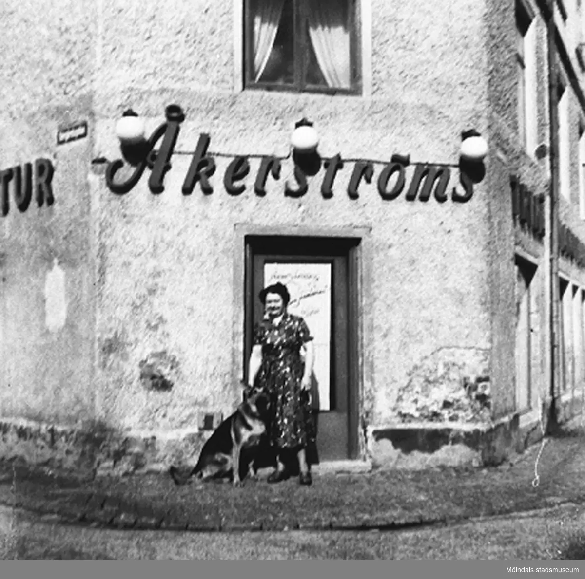 En kvinna och en schäfer står utanför Åkerströms manufakturaffär på Sörgårdsgatan 2 i Krokslätt. Okänt årtal.