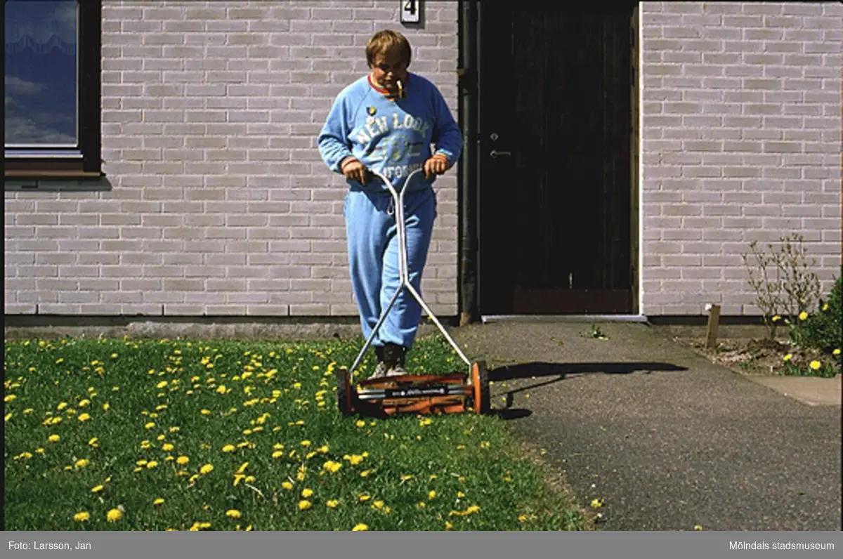 En person klipper gräset utanför en gruppbostad vid Stretereds vårdhem, 1980-talet.