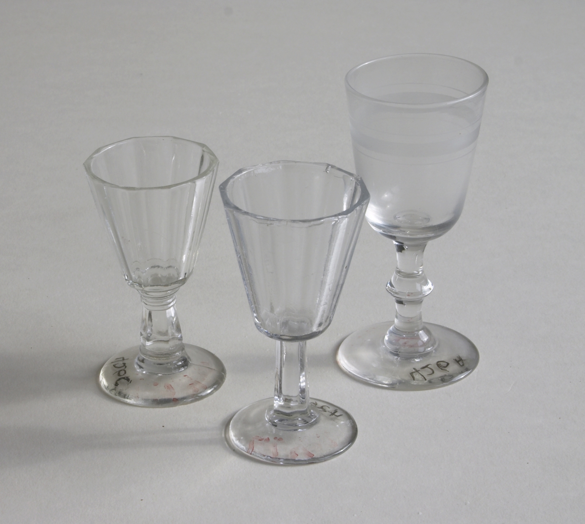 3 drammeglass. Runde på fot. Det ene glasset har en matt ring rundt toppen, de to andre har en form for folder i glasset. 