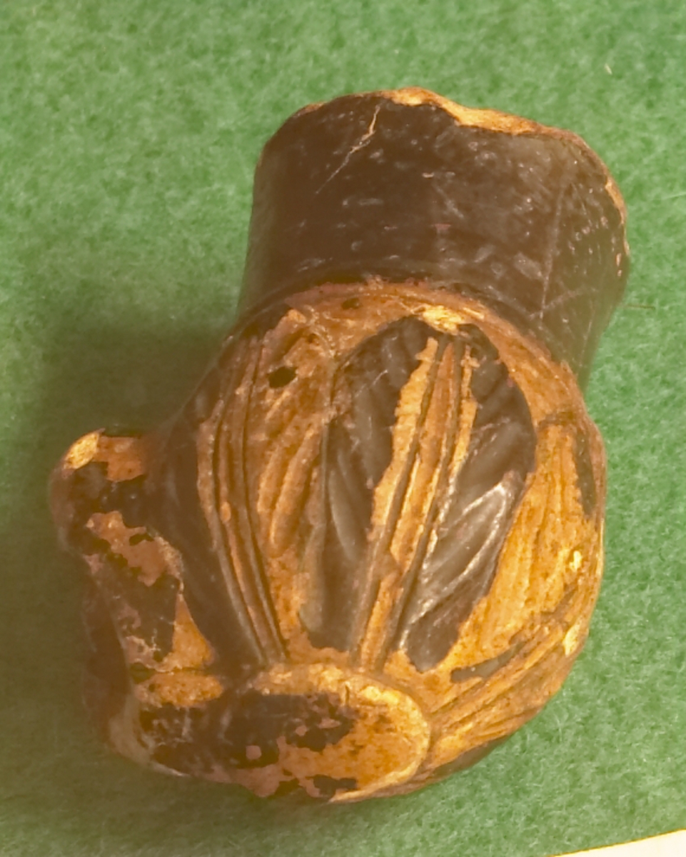 Sjølve pipa mangler. Laget av bein og har utskårne blader nederst. Øverst en rund brun ring, har ellers en brun-gul farge.