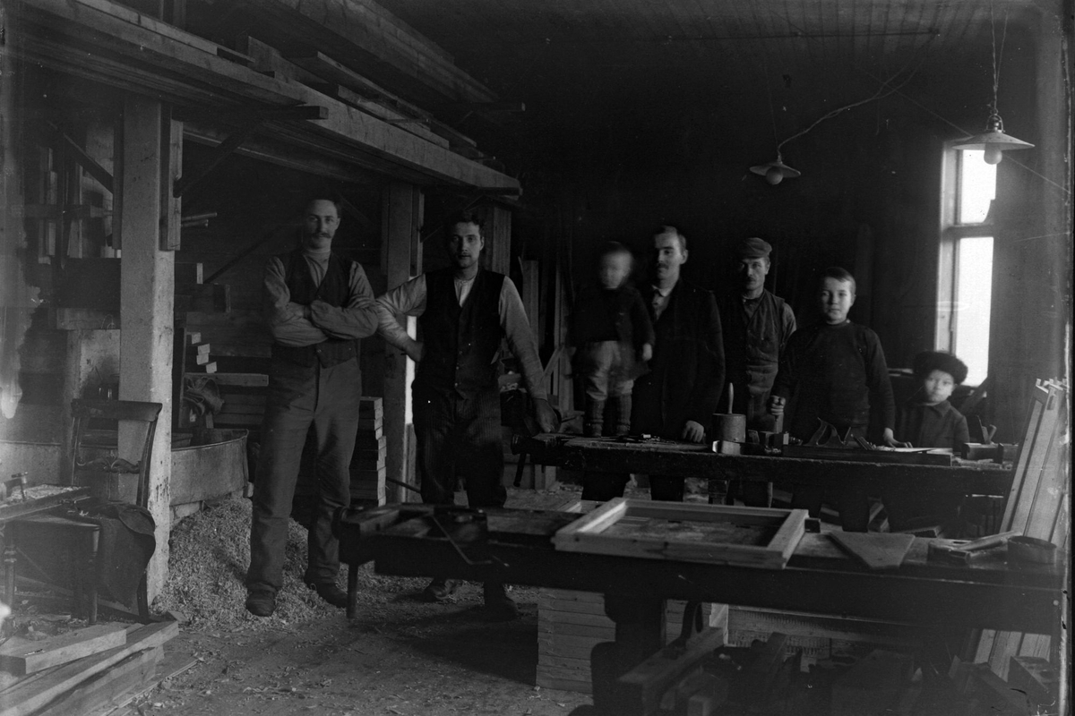 Gruppeportrett av arbeidere på et snekkerverksted. Barn til høyre.