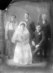 Studioportrett i helfigur av et brudepar med familie.