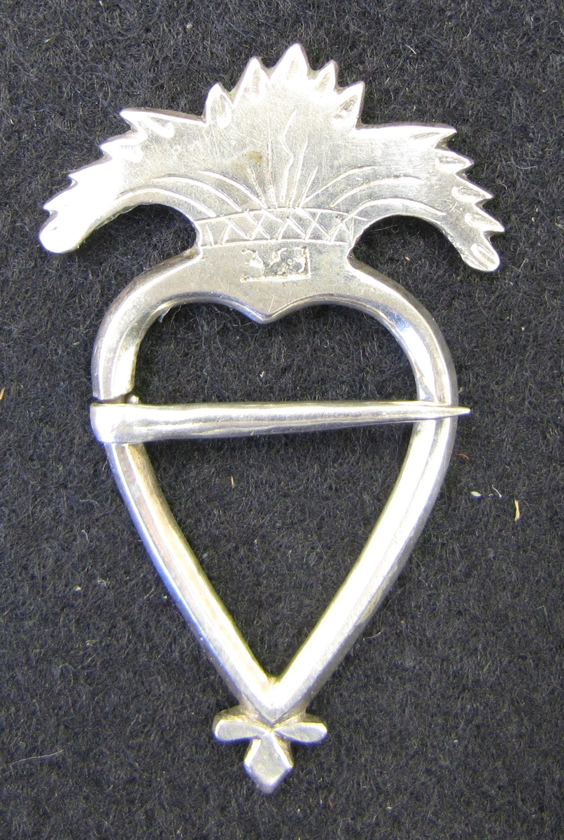 Ett litet hjärtformigt silverspänne krönt med tre flikar.