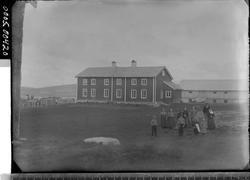 En gruppe mennesker foran et våningshus og låve.