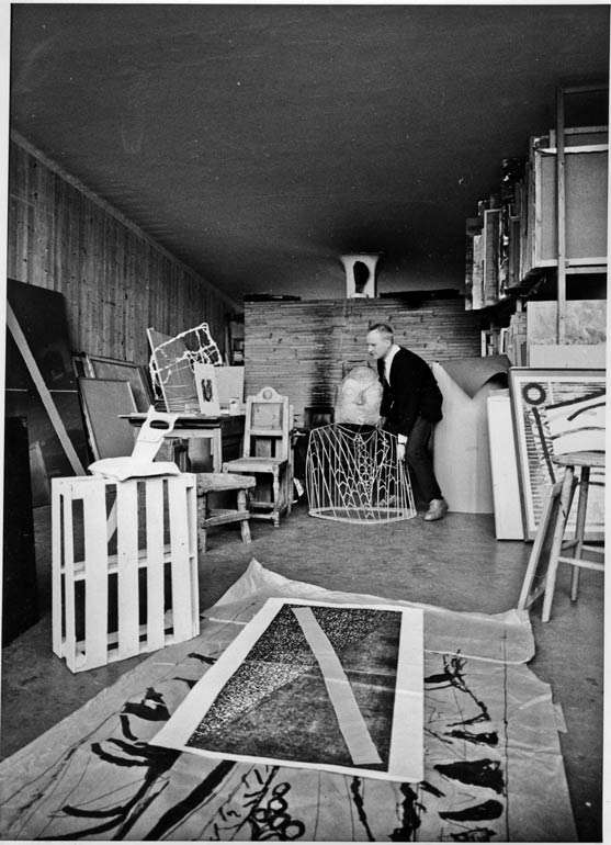 Ludvig Eikaas i sitt atelier med: stor skisse til Asfaltmann, liten skisse til Asfaltmann (EG 168), Ex Libris (EG 273), Bækkelund skulptur (EG 274), Å lage en skulptur... (EG 164), Airport (EG 627 eller EG 751) "Businessmann" (1970) og "Flagg"-grafisk blad.