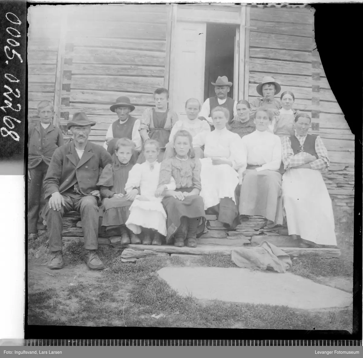 Gruppebilde av fire menn, syv kvinner og fire barn ved et inngangsparti.