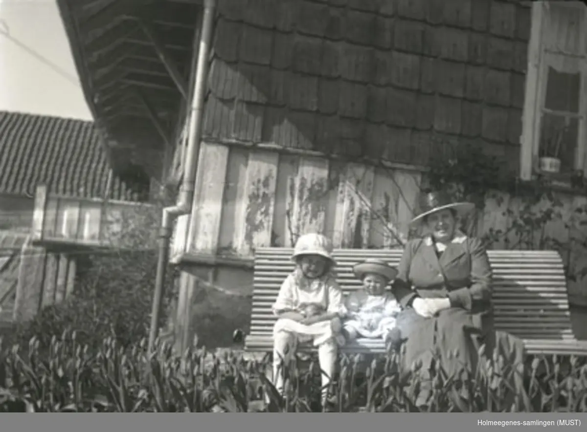 En voksen kvinne og to barn sitter på en hagebenk på Holmeegenes i Stavanger. Tulipanbed i forgrunnen.