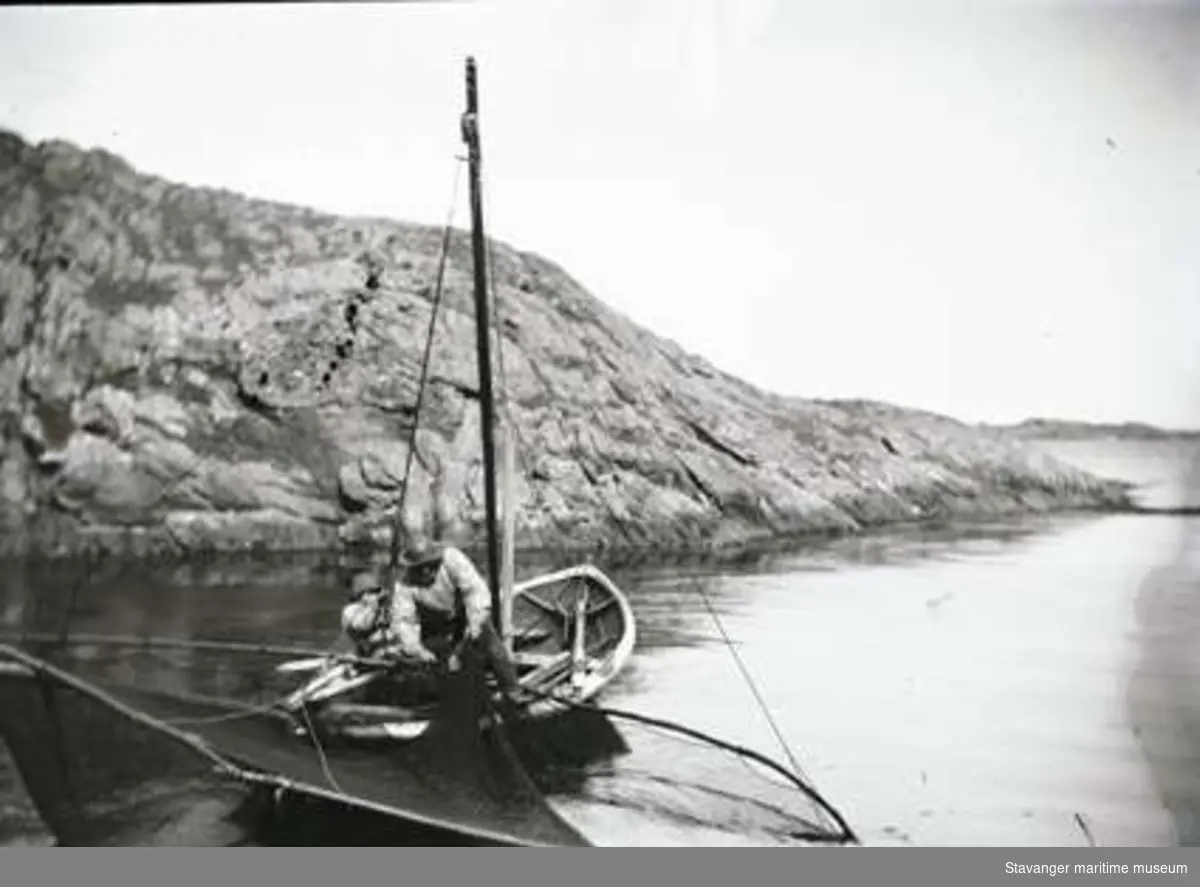 Glipfiske fra liten seildreven fiskebåt med to mann ombord. Mannen som drar garnet er sannsynligvis Lars Hansen Haaland, Lauritz Haalands far.