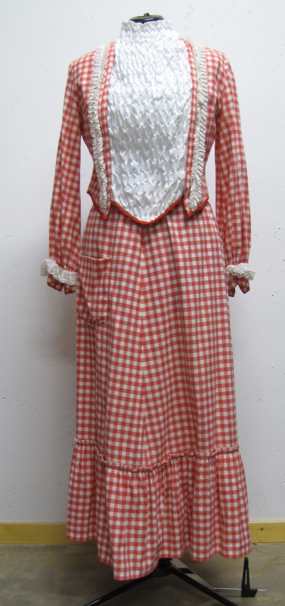 Klänning i två delar, kjol och överdel. Klänningen är sydd i röd-vit rutigt tyg. Kjolen är lång med en bred volang nertill och knäppes med hakar i ryggen. Överdelen har hög krage och ett vitt stycke framtill. Överdelen är försedd med hakar och dragkedja.

Klänningen ingick som fridaklänning i  teaterspelen, denna sydd till Inga Maj Holmlund (f. 1920-09-09). De användes till hennes roll  som en av Fridorna i Birger Sjöbergsspelen, kallad ''Lilla Paris - Ett Birger Sjöbergspel i Vänersborg''.

Spelet arrangerades åren 1980-1985 i juni månad vid midsommarviken, nedanför Skräcklestugan , Vänersborg. Föreställningen spelades, fredag, lördag, söndag med 2 föreställningar lördag-söndag.

Efter att spelen tog slut fick Ann-Marie Andersson (f.1930-07-17) överta klänningen. Hon var sambo med Frank Johnsson och när Frank var ute och framträdde som Birger Sjöberg och sjöng hans visor, kunde Ann-Marie bistå honom i rollen som Frida.

Frank Johnsson (1939-01-24 - 2003-09-11) var lärare, främst i matamatik och biologi. Från 1971 undervisade han på Huvudnässkolan. Mest var han känd för sången och musiken. Genom nämda Fridaspel på Skräcklestugan kom han att förknippas med Birger Sjöbergs och han tolkade gärna den store Vänersborgs-sonen.
