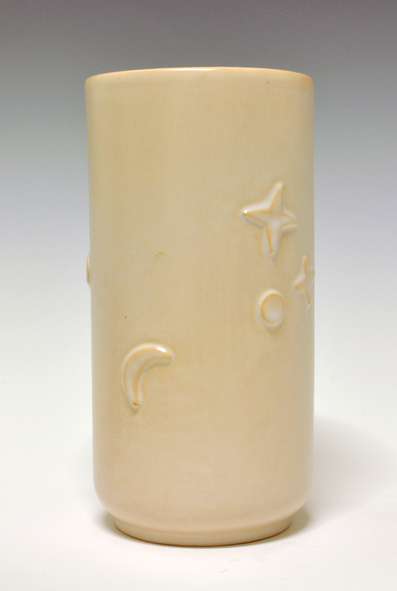 Vase av "keramikk". Sylinderform med inntrukket fotrand. På sidene stjerner, månedsigder og sirkler i relieff. "Lyserødbeige" glasur. 
Modell: R.5010k
Dekor: 1002