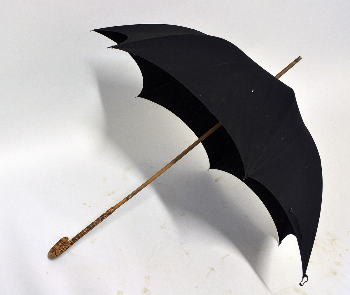 Sort stoffparaply med bøyd håndtak av tre.