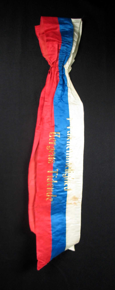Begravelsessløyfe i hvit, rød og blå silke med tekst i gull.