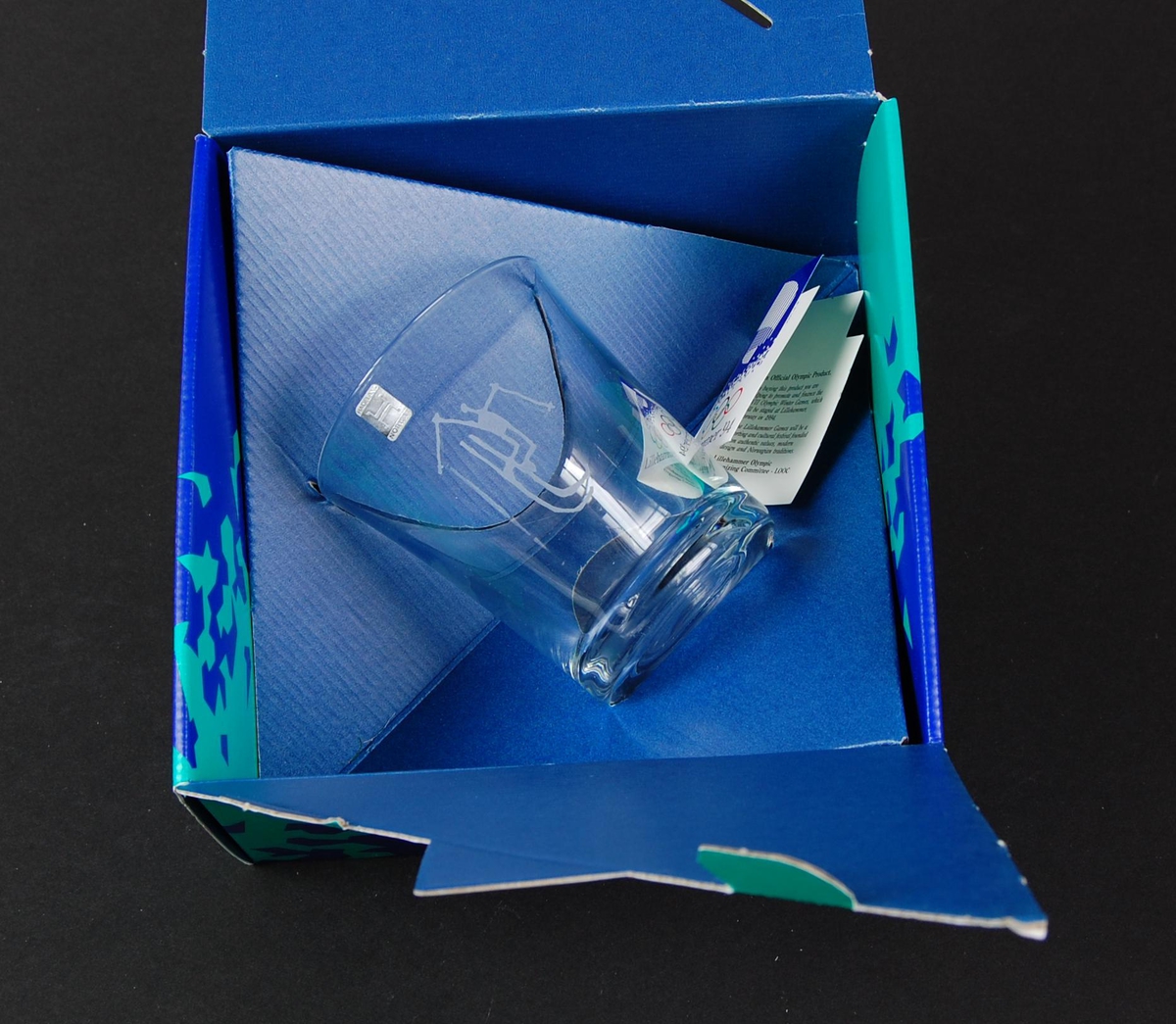 Whiskyglass med piktogram for sportsgrenen freestyle, kulekjøring. Glasset ligger i en blå og grønn pappeske med krystallmønster. Krystallmønsteret inngikk i LOOCs designprogram. På esken er det også en logo for de olympiske vinterleker på Lillehammer i 1994. 