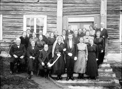 Gruppebilde, bryllup, brudepar, bryllupsgjester, hus i bakgr