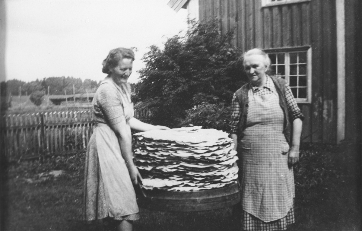 Flatbrødbakst  på Hovin. To kvinner bærer flatbrødstablen mellom seg.