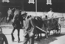 Menn med to hester og vogn av flettet kurv på gårdstun.