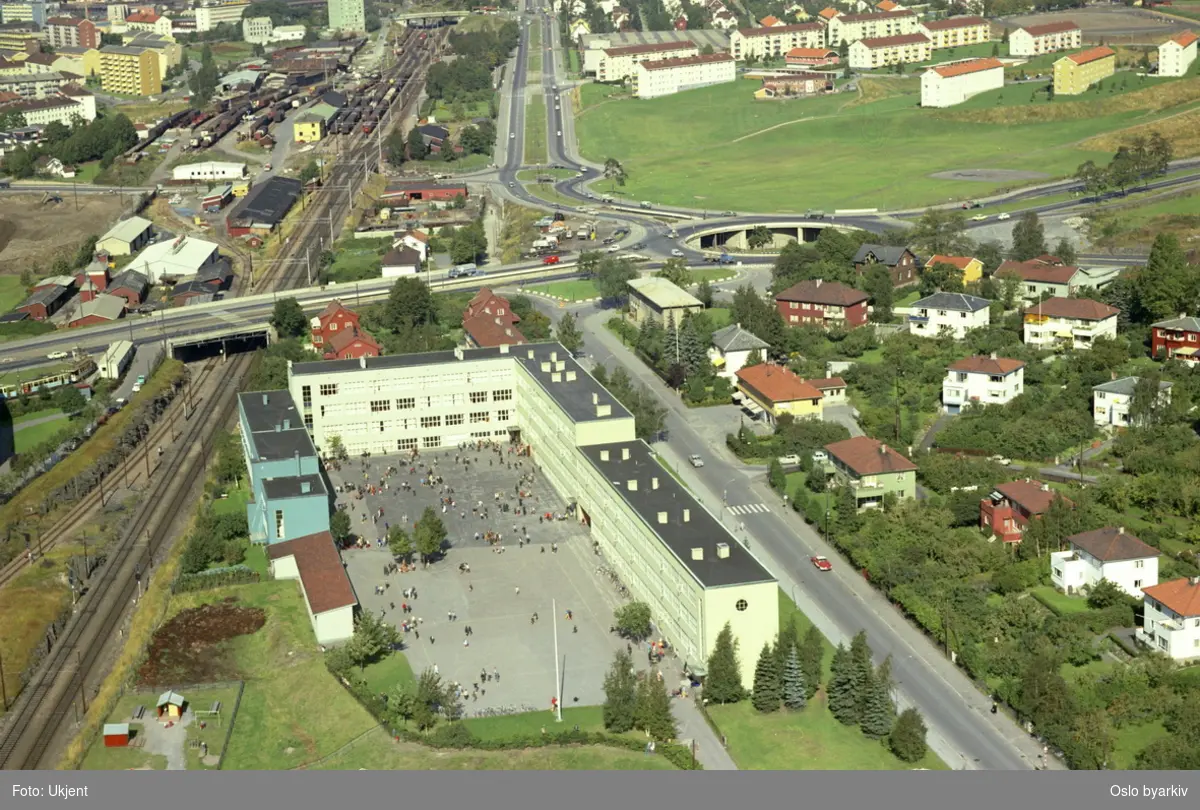 Sinsen skole. Jernbanesporet til Gjøvikbanen til venstre og Lørenveien til høyre for skolen. Trondheimsveien og Ringveien møttes i Sinsenkrysset lenger bak. Grefsen jernbanestasjon og boligblokker på Disen i bakgrunnen. (Flyfoto)