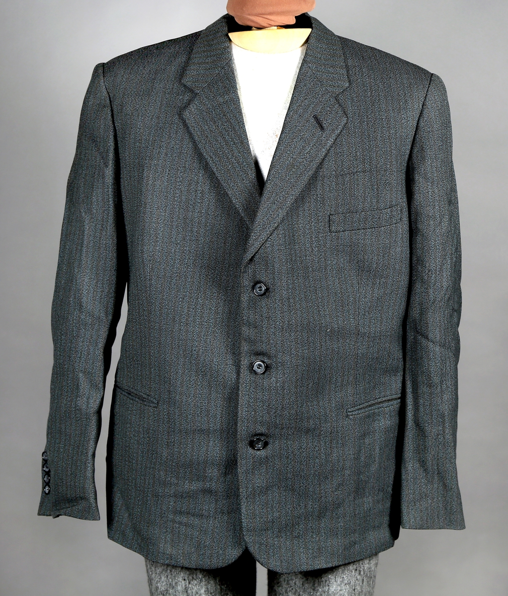 Dress med gråstripete mønster i stoffet, enkelt spennet jakke som kneppes med tre knapper. Jakka er silkefôret, unntatt ermene. Bukse med fire lommer. 