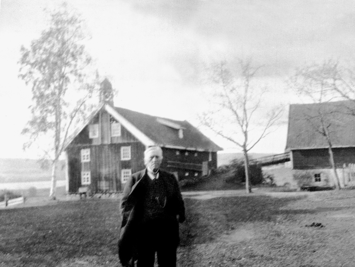 Even Arnt Nilsen Gjestvang (1829-1927) på tunet på Kise Mellem. I bakgrunn stabburet med matklokke som ble bygd i 1847.