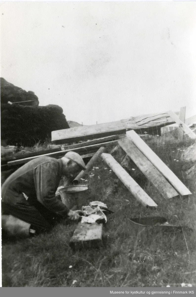 Georg Adriansen jobber med fisk. I bakgrunnen familiens gamme. Gamvik 1945.