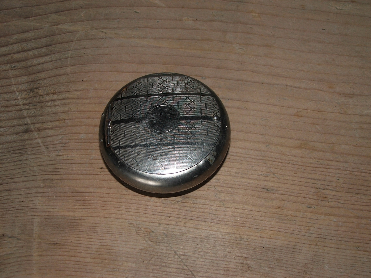 En rund beholder av metall med lokk, inngravert mønster på lokket