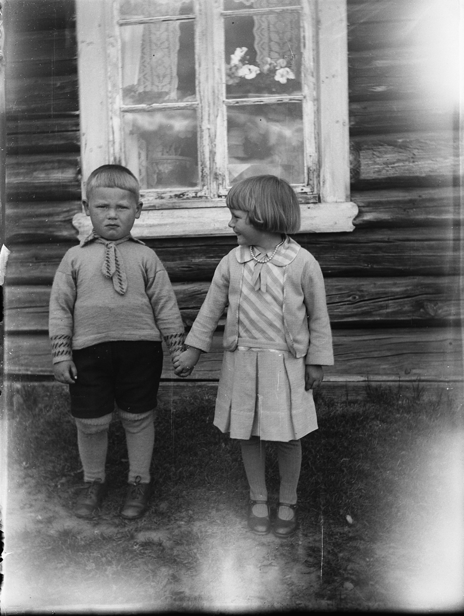 To ukjente barn holder hverandre i hendene foran et ukjent hus. 