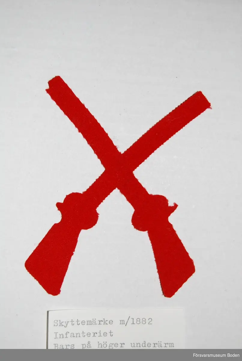 Två korslagda gevär av rött kläde. Utmärkelsetecken för skjutskicklighet som syddes fast på uniformens högra underärm.