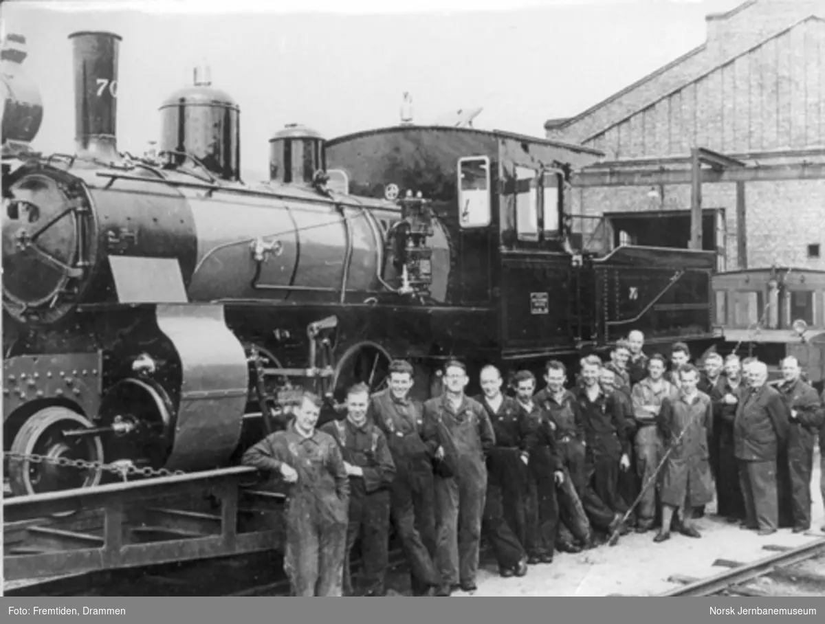 Nyoppusset damplokomotiv type XXIIIa nr. 70 opplastet på spesialvogn på verkstedet Sundland før forsendelse til Jernbanemuseet, med verkstedarbeiderne oppstilt foran