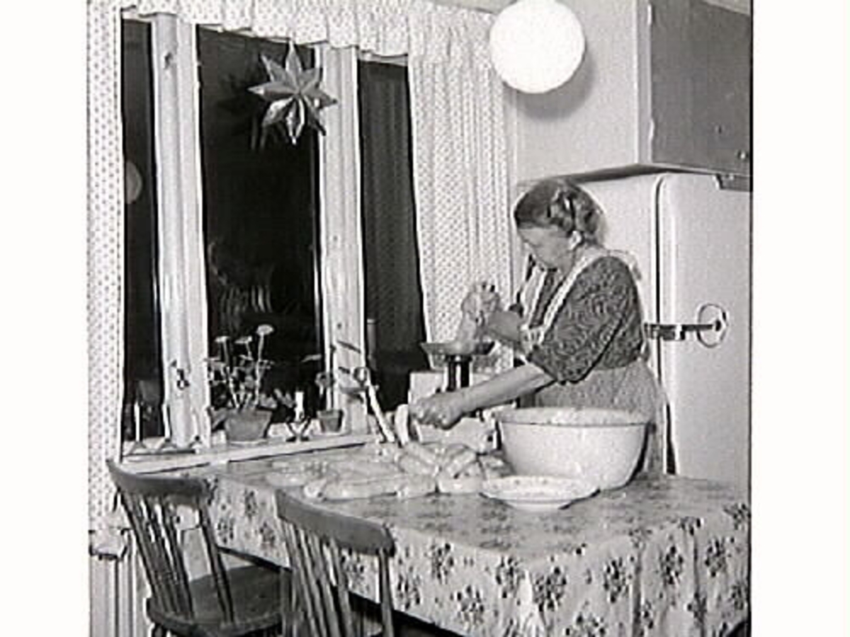 Maria Öberg stoppar korv vid köksbordet. Slaktet görs iordning inför jul. Bakom henne syns ett kylskåp.